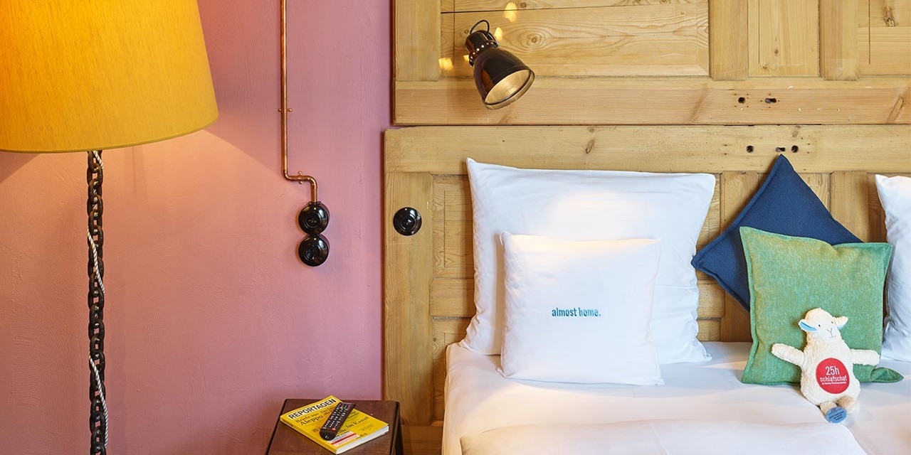 Gemütliches Schlafzimmerinterieur mit wandmontierter Nachttischlampe und dekorativen Kissen auf dem Bett