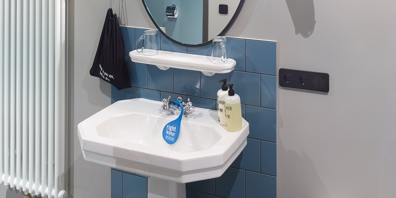 Modernes Badezimmer mit weißem Waschbecken, blauen Fliesen und schwarzer Steckdose an der Wand