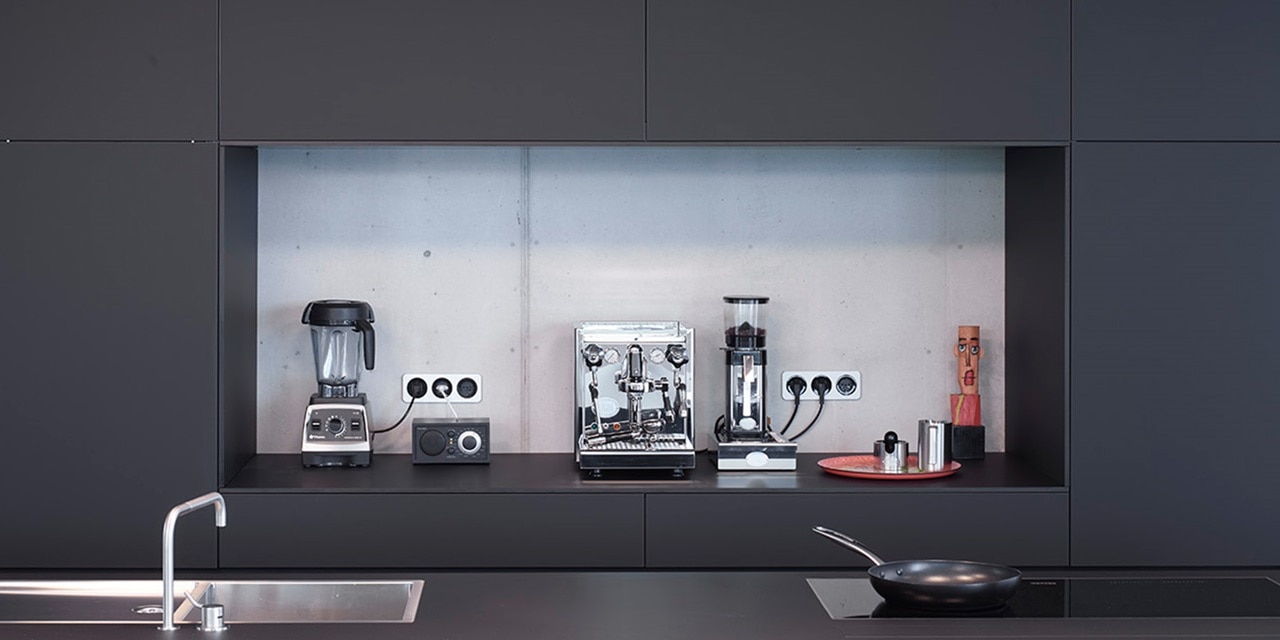 Moderne Küche mit Elektrogeräten, darunter Mixer, Kaffeemaschine und Steckdosen an der Wand