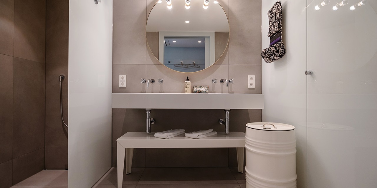 Modernes Badezimmerinterieur mit Doppelwaschtisch und Spiegel, wandmontierten Wasserhähnen, Beleuchtungskörpern und Glasduschabtrennung