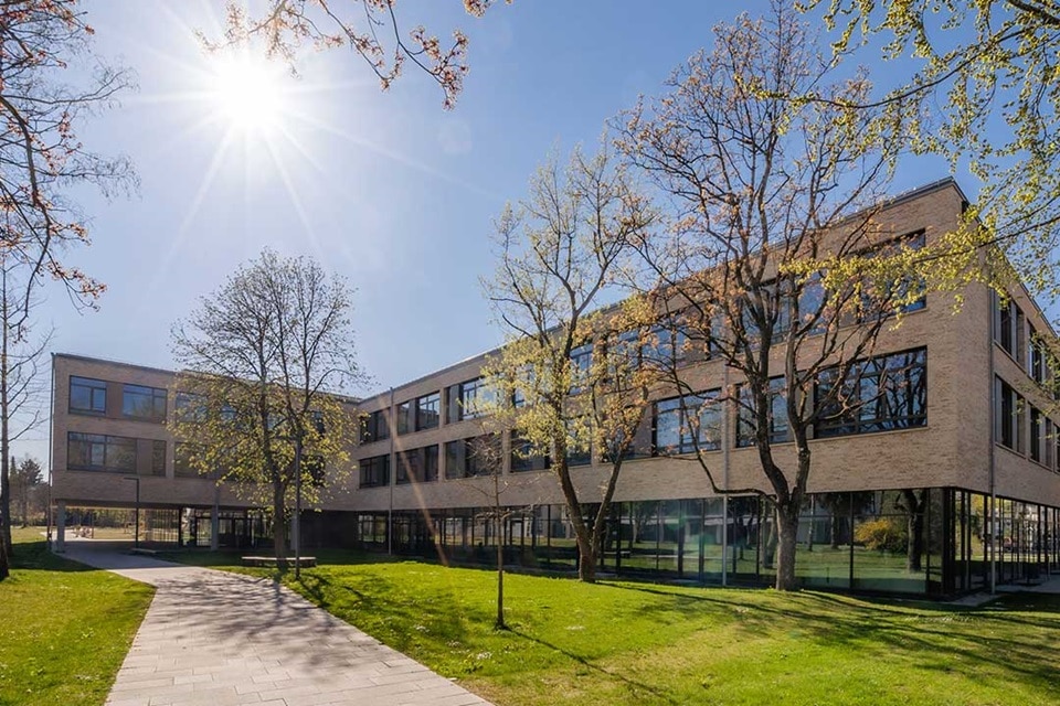 Modernes Bürogebäude mit großen Fenstern und grüner Landschaftsgestaltung an einem sonnigen Tag