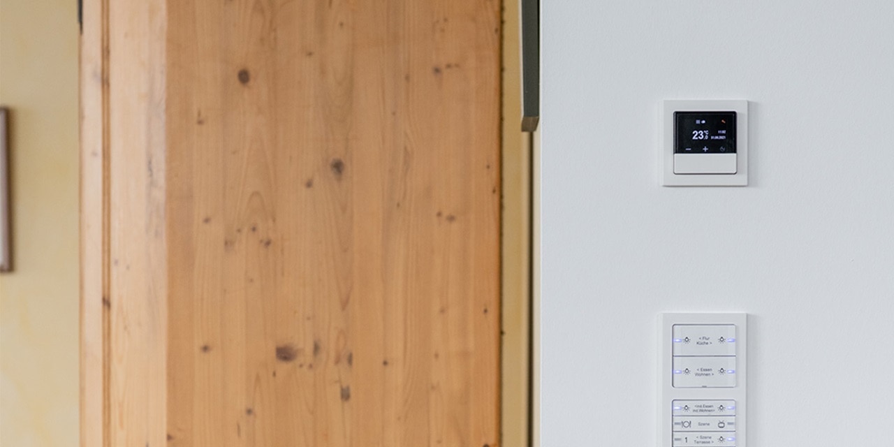 Moderner intelligenter Thermostat und Steuerungspanel für Hausautomation an der Wand neben einer Holztür