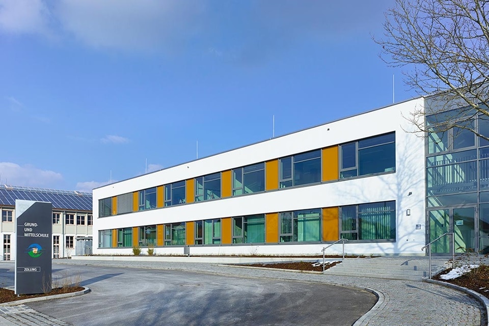 Modernes Schulgebäude mit Solarmodulen auf dem Dach und bunten Fenstern unter blauem Himmel