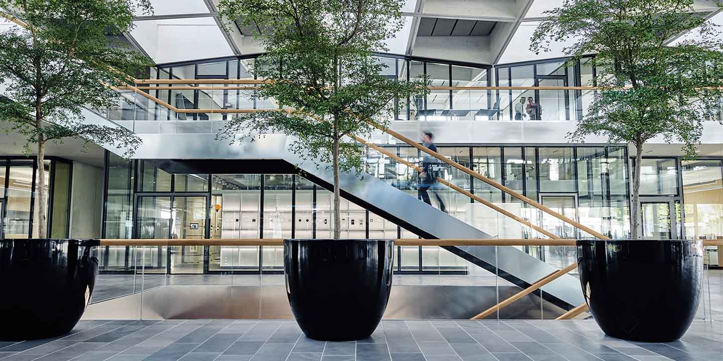Moderne Bürolobby mit großen Pflanzgefäßen, offenen Treppenhäusern, Glasgeländern und laufenden Personen