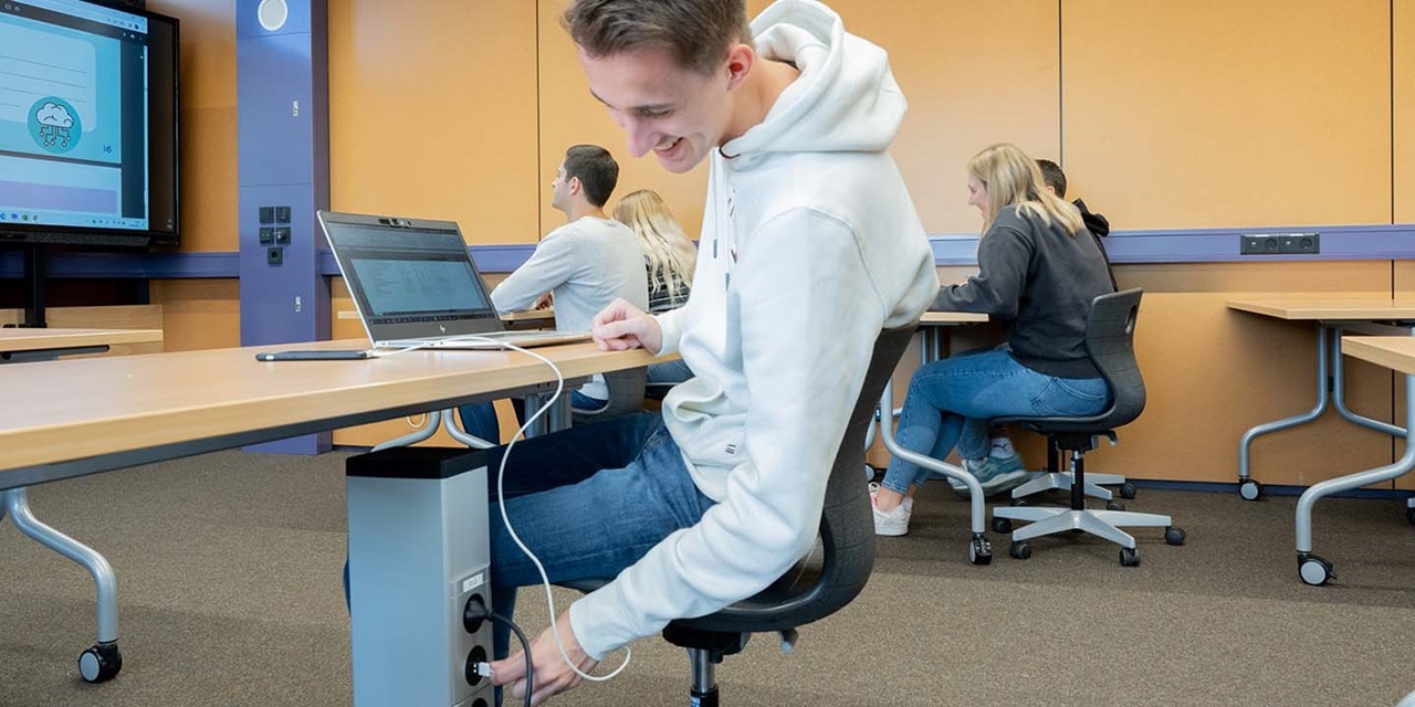 Person benutzt einen Laptop in einem Klassenzimmer mit eingebauten Tischelektrizitätsversorgungen