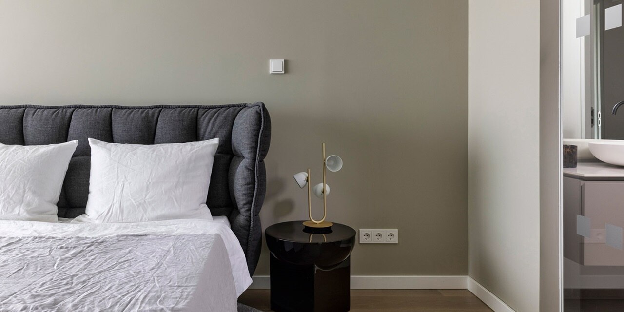 Modernes Schlafzimmer mit stilvollem Kopfteil, dekorativer Tischlampe und Steckdosen an der Wand