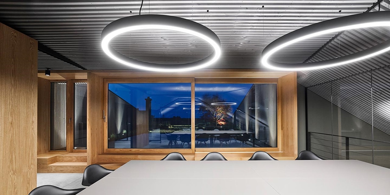 Modernes Bürointerieur mit runden LED-Pendelleuchten, Konferenztisch und großen Fenstern bei Nacht