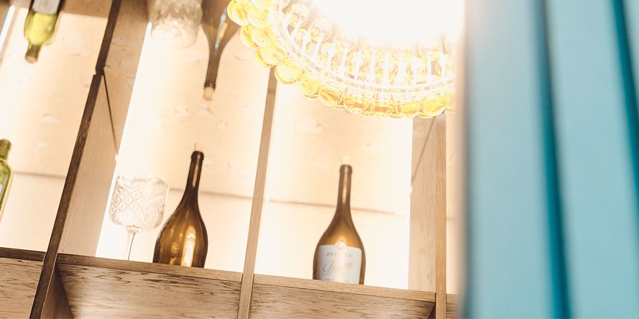 Eleganter Kronleuchter mit gelben Lichtern über einem Holzregal mit dekorativen Flaschen und Gläsern