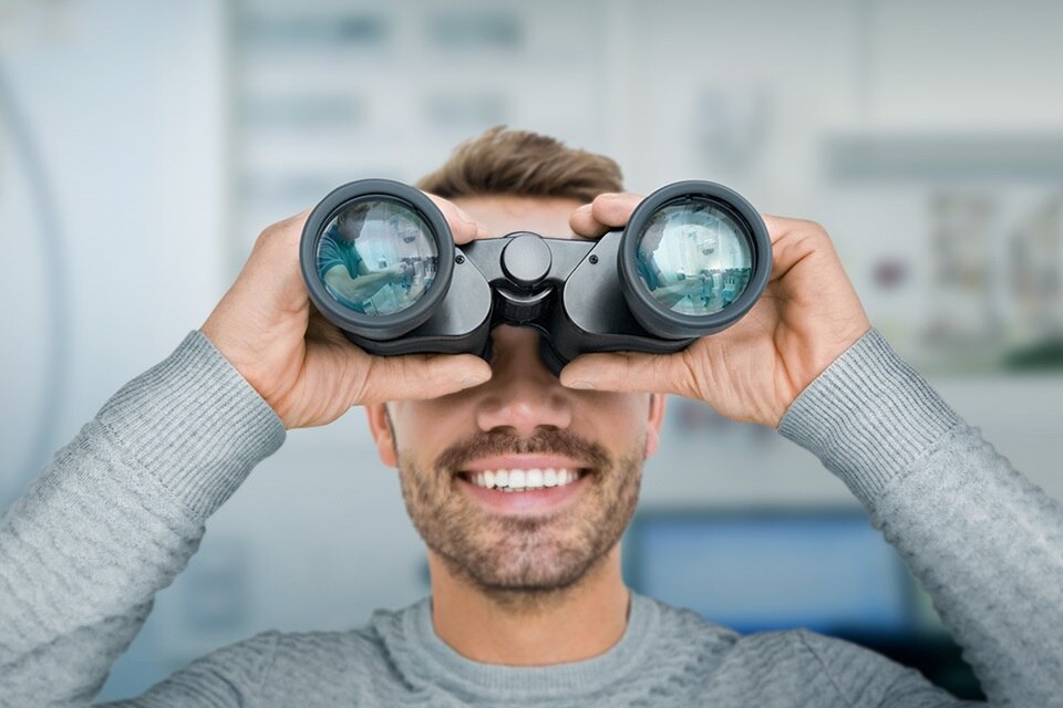 Fronansicht auf Mann, der lächelnd durch ein Fernglas schaut. 