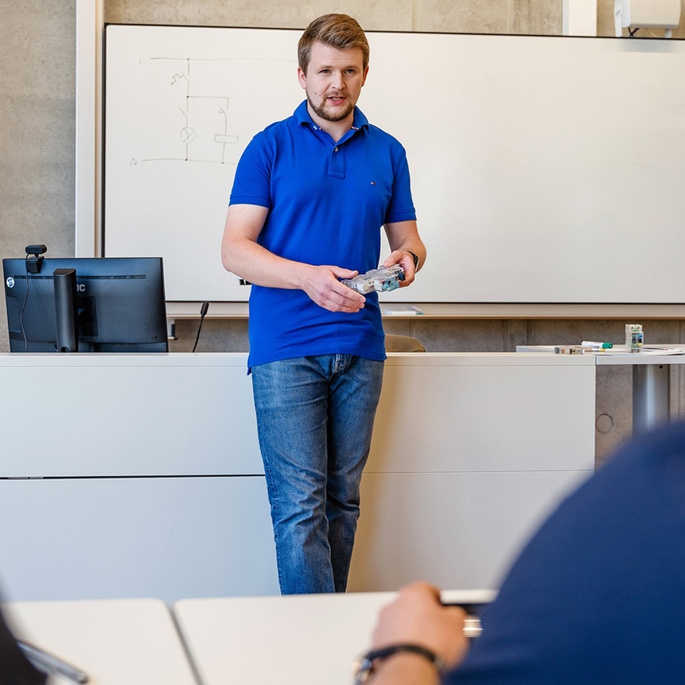 Person führt eine Schulung mit einem elektrischen Bauteil in einem Klassenzimmer durch
