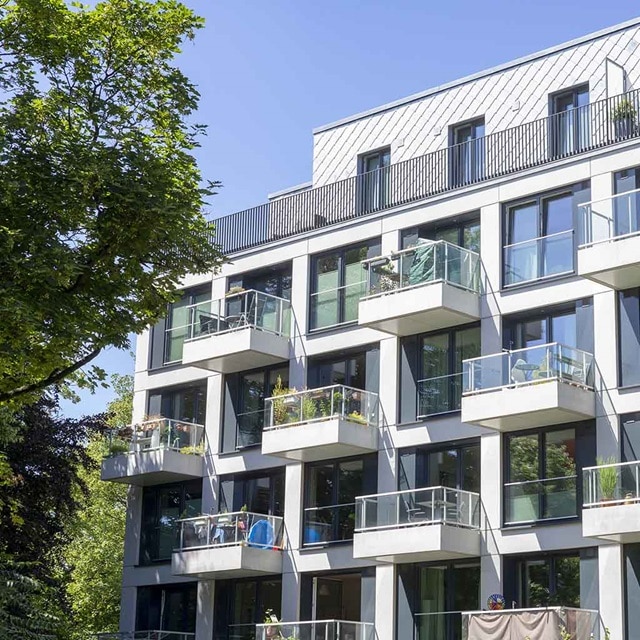 Modernes Wohngebäude mit Balkonen und großen Fenstern in einem städtischen Gebiet, umgeben von Grün