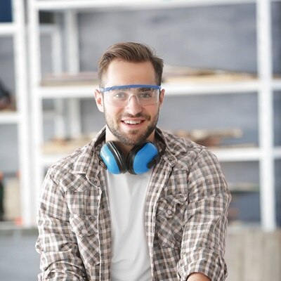 Person in einer Werkstatt mit Schutzbrille und Kopfhörern um den Hals