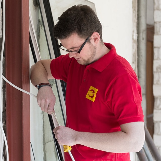 Elektriker installiert Kabel in einem Gebäude, trägt ein rotes Hemd mit Logo