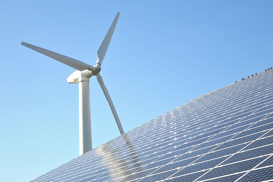 Solarmodule mit einer Windturbine vor klarem blauem Himmel, Darstellung von erneuerbaren Energiequellen
