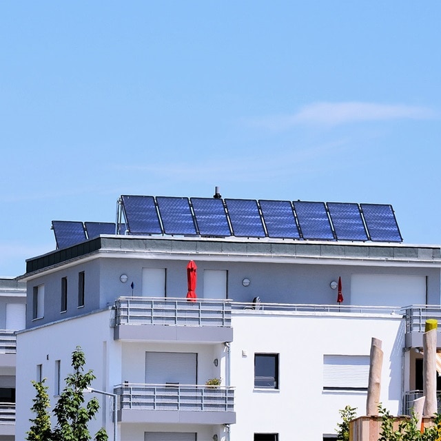 Auf dem Dach eines modernen weißen Wohngebäudes installierte Solarmodule unter einem klaren blauen Himmel