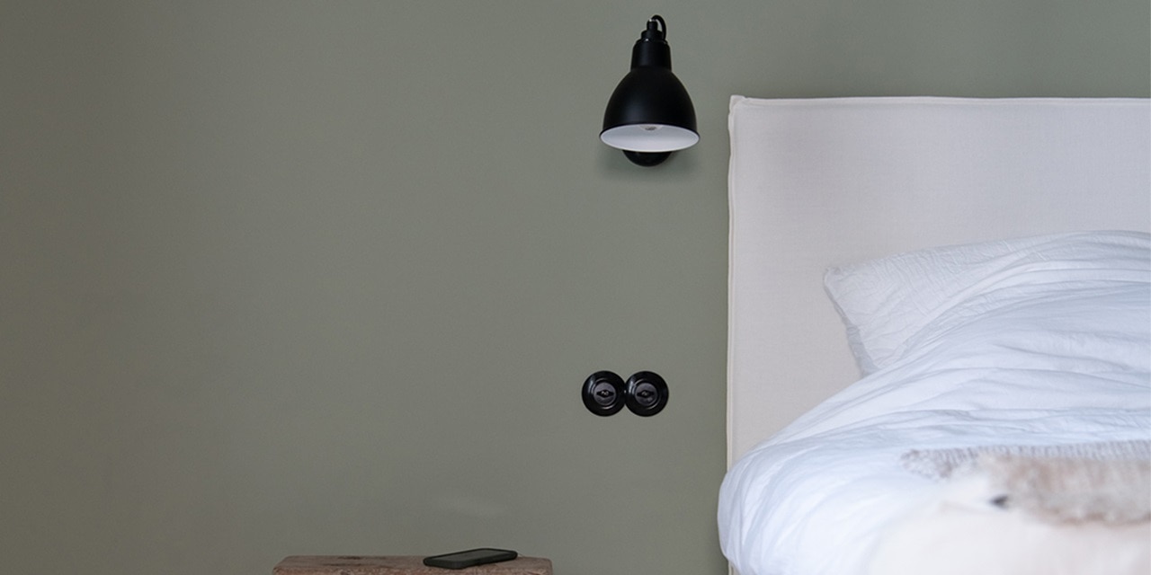 Minimalistisches Schlafzimmer mit Wandlampe und Doppelsteckdose an grüner Wand