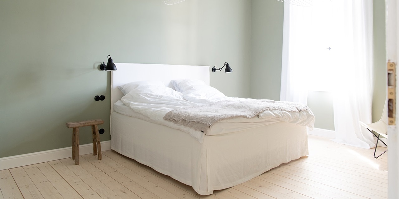 Minimalistisches Schlafzimmerinterieur mit weißem Bett, Wandlampen und Holzboden