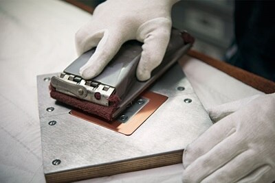 Person mit Handschuhen führt eine Qualitätskontrolle an einer elektrischen Komponente mit einem Multimeter durch