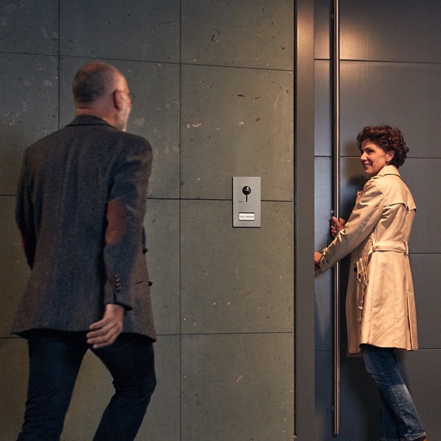 Person benutzt ein modernes Zugangskontrollsystem neben einem Aufzug, während eine andere Person vorbeigeht
