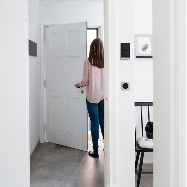 Person öffnet eine weiße Tür mit intelligenten Haussteuerungspanelen an der Wand