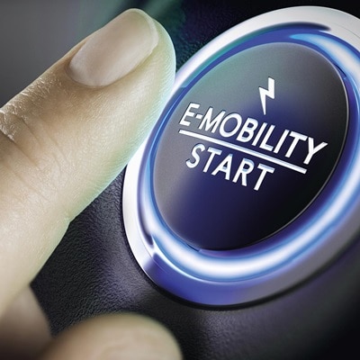 Startknopf mit der Aufschrift E-Mobility und einem Finger, der den Knopf drückt. 