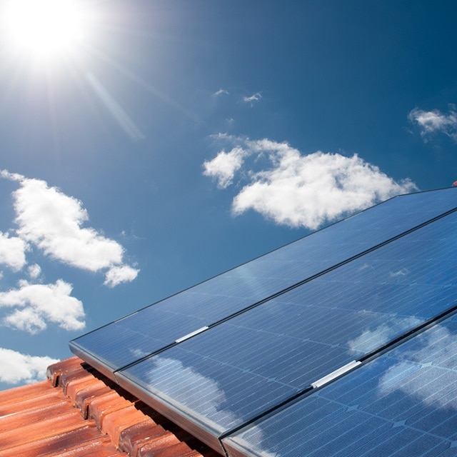 Solarmodule auf einem Dach vor blauem Himmel und Sonne im Hintergrund