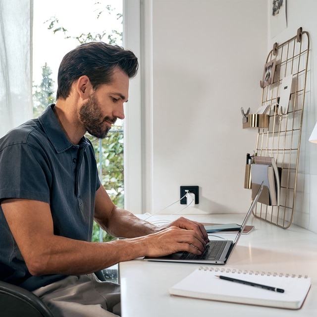 Person arbeitet an einem Laptop im Heimbüro mit einem an der Wand montierten Gitter-Organizer und Steckdose im Hintergrund