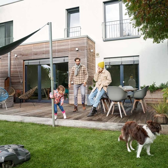 Familie genießt die Zeit in einem modernen Garten mit Gartenmöbeln und einem Rasenmähroboter