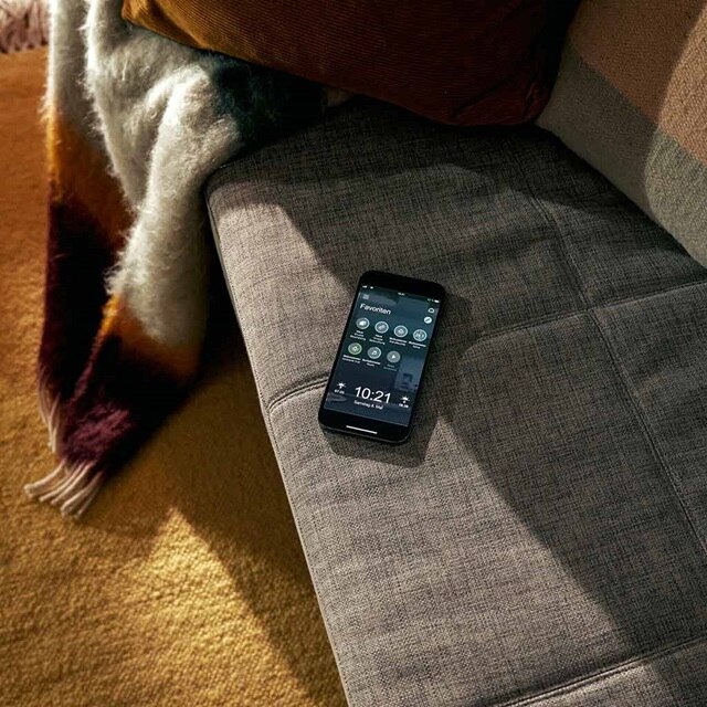 Smartphone mit Hausautomatisierungs-App auf einem Sofa in gemütlicher Raumatmosphäre