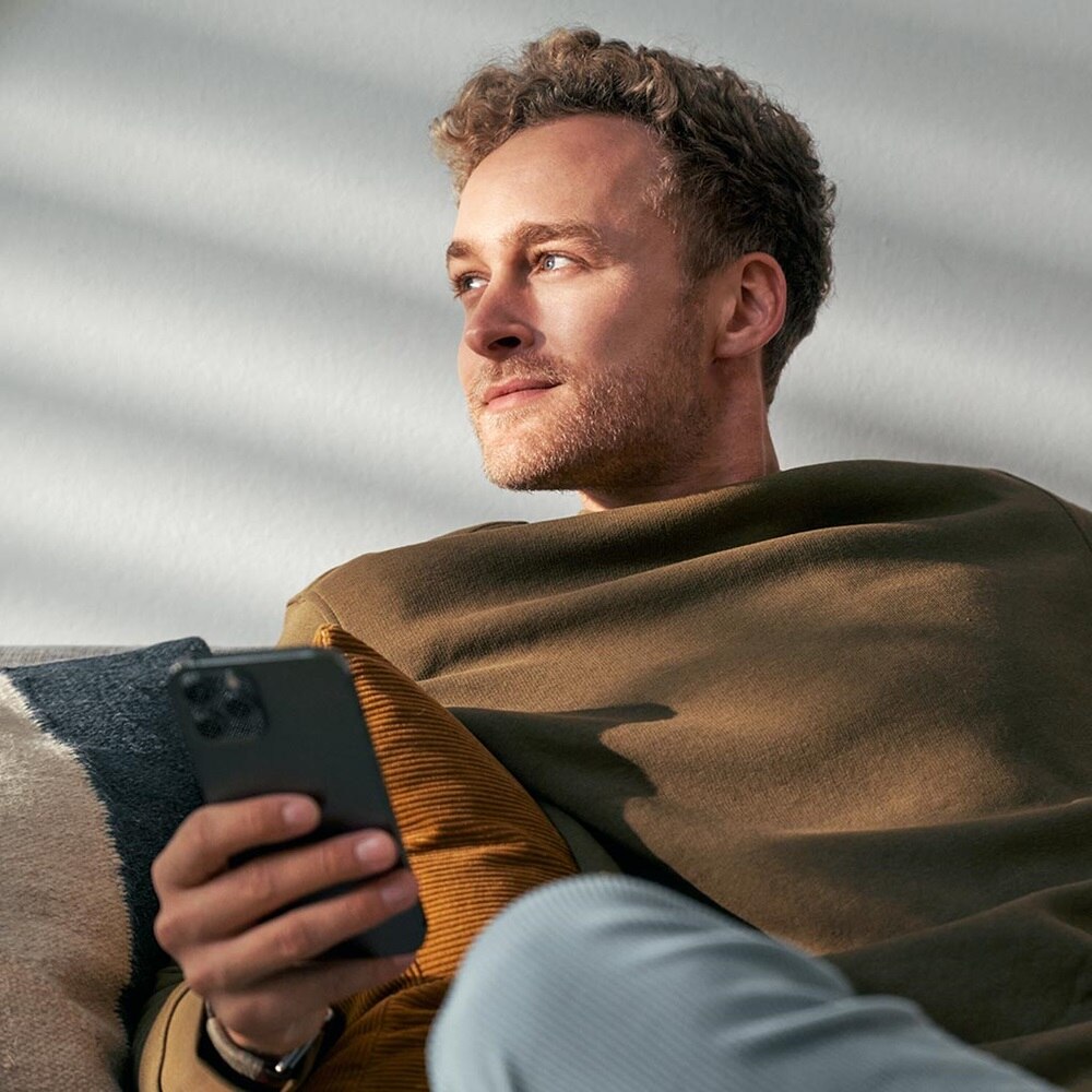 Person entspannt sich und hält ein Smartphone, blickt nachdenklich weg