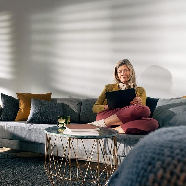 Person sitzt auf einem Sofa und verwendet ein Tablet in einem hell erleuchteten Wohnzimmer mit moderner Einrichtung