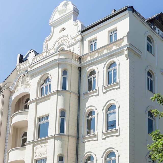 Verzierte Fassade eines weißen historischen Gebäudes mit architektonischen Details unter einem klaren blauen Himmel