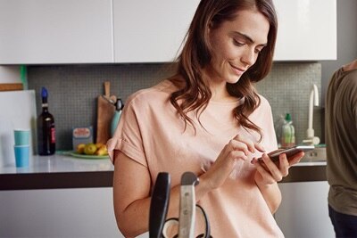 Eine Frau steht mit dem Handy in der Hand in der Küche