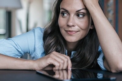 Eine Frau sitzt mit Tablet am Tisch.