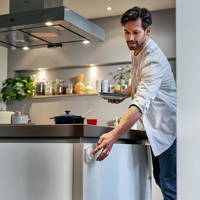 Person in einer modernen Küche beim Öffnen einer Schublade mit Tellern in der Hand