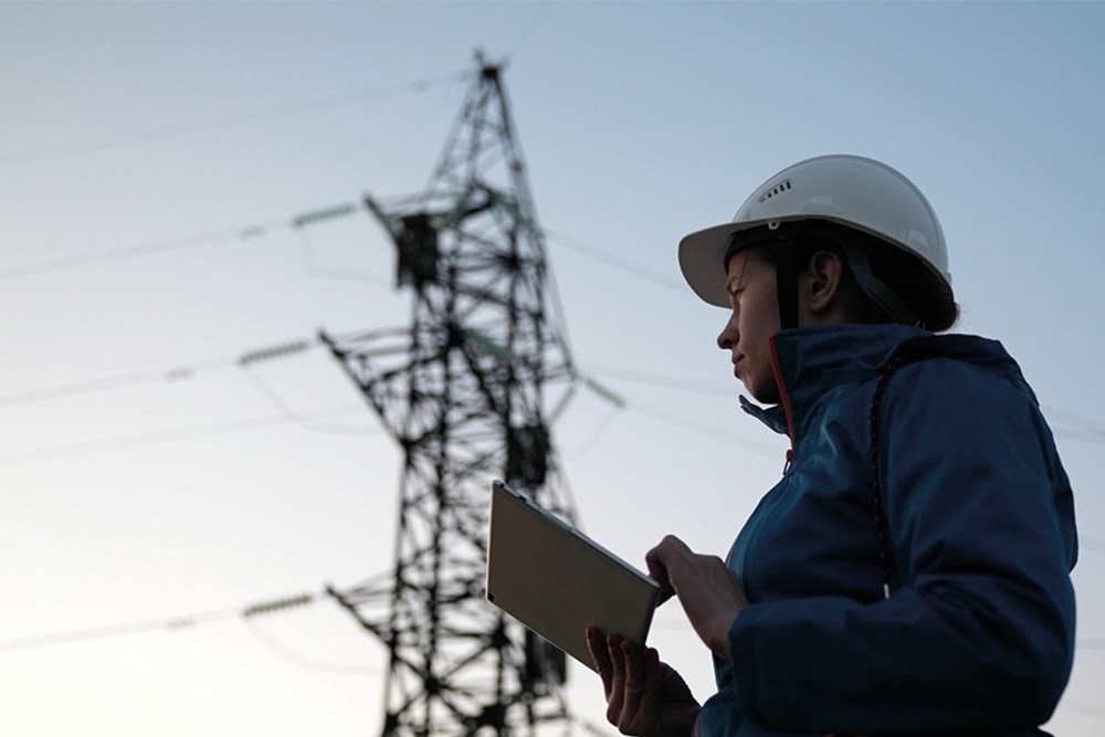 Energy engineer with tablet in front of power pole