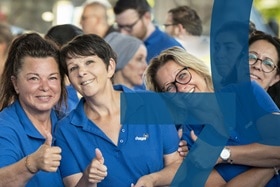 Mitarbeitende der Hager Group in blauen Poloshirts lächeln und zeigen Daumen hoch bei einer Firmenveranstaltung.