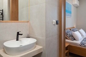 Hager group Modernes Badezimmer mit beigen Fliesen und holzfarbenen Elementen mit Blick ins Schlafzimmer