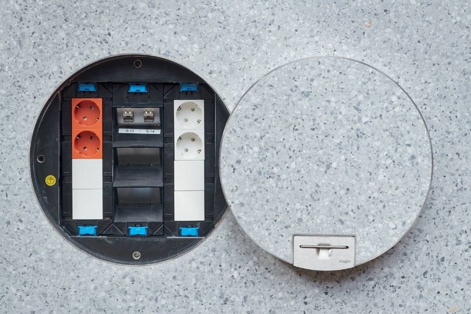 Open floor socket with modular inserts for power and data beside its cover on a terrazzo floor surface