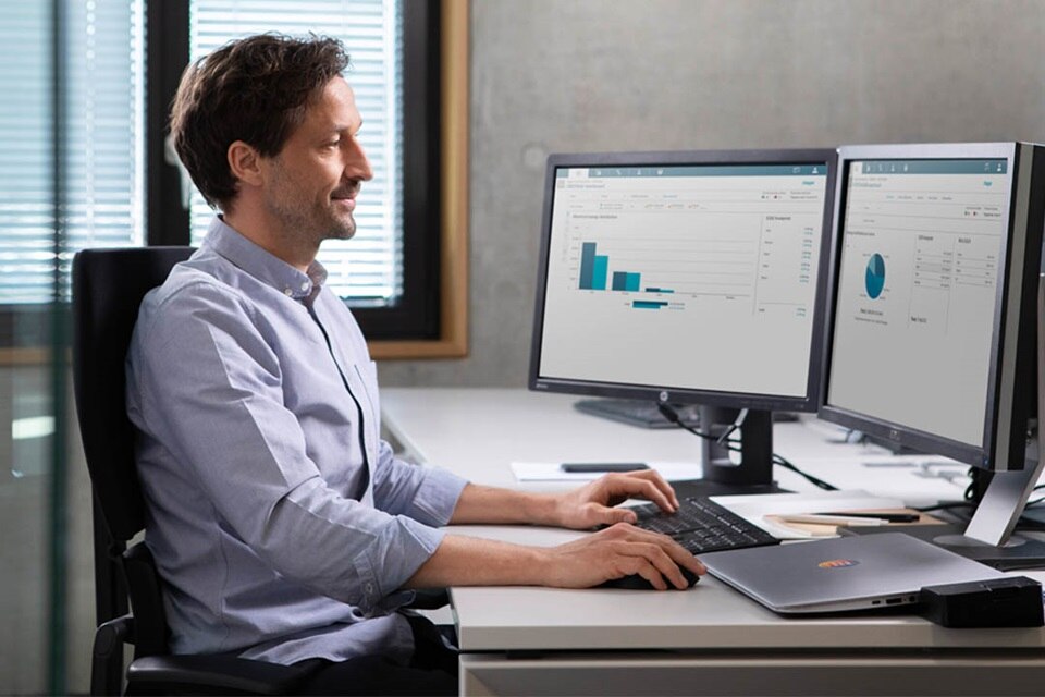 Professional in office environment using dual monitors with data analysis charts on screen