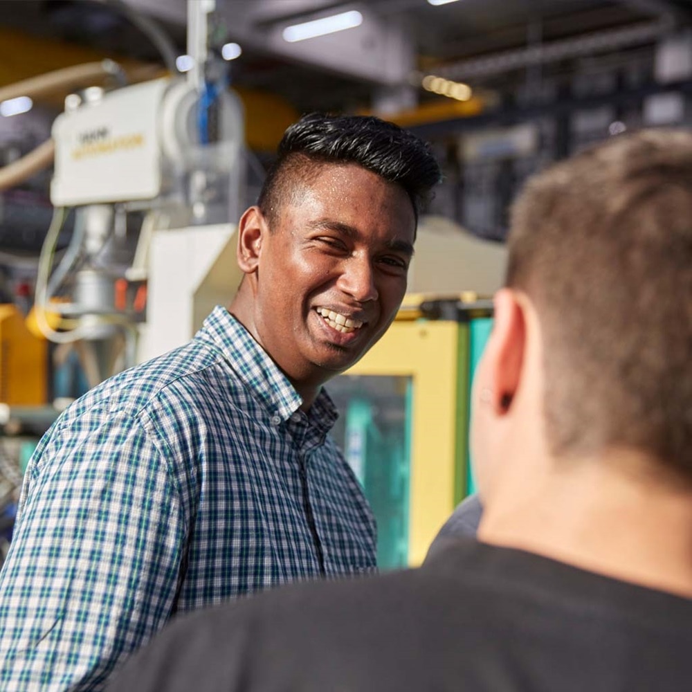 Person smiling at a colleague in an industrial setting with machinery in the background