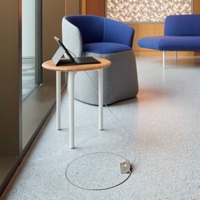 Modern office waiting area with laptop on wooden side table and electrical floor outlet