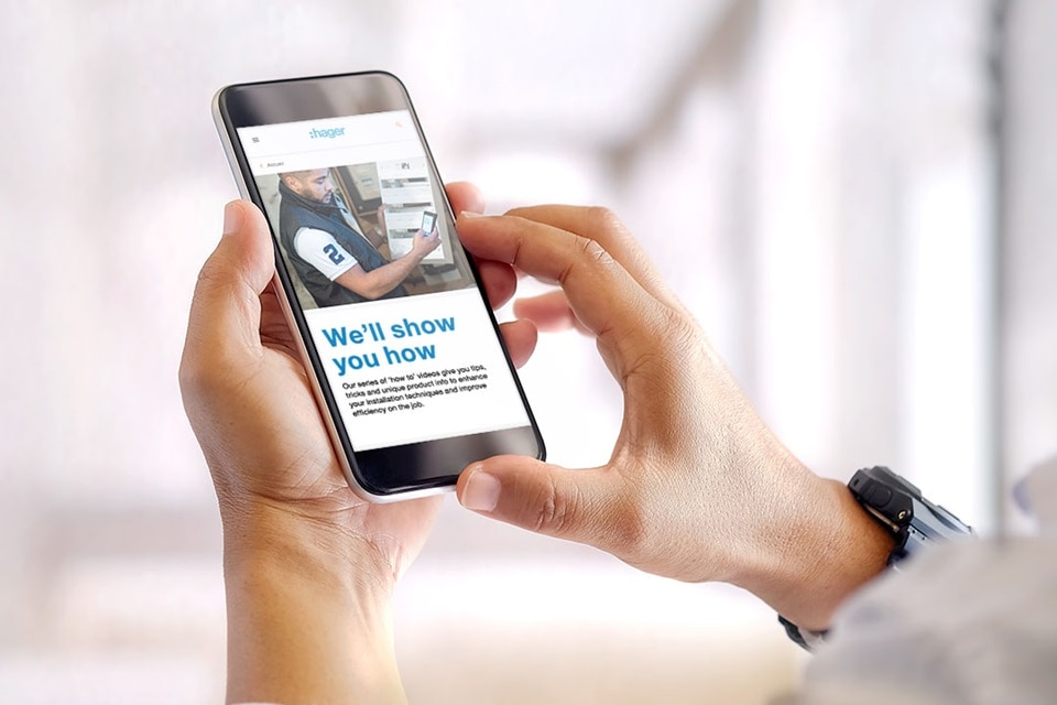 Person holding a smartphone with Hager website displayed, showing electrical solutions and services