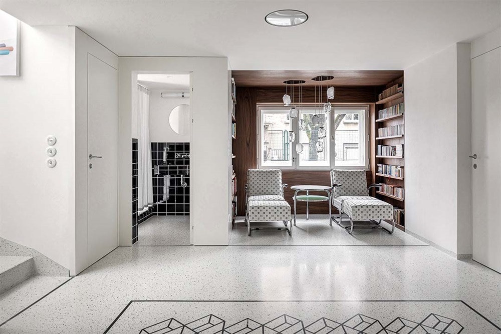 hager group White flow-lined hallway with couches in an adjoining room with wood-coloured wall