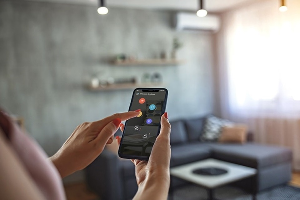 Persona utilizando una aplicación de móvil para el control de la automatización del hogar en una sala de estar moderna