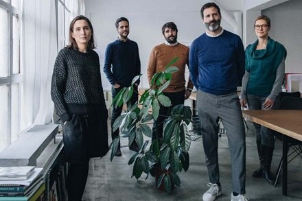 Grupo de profesionales de pie en un ambiente de oficina con iluminación natural y plantas verdes