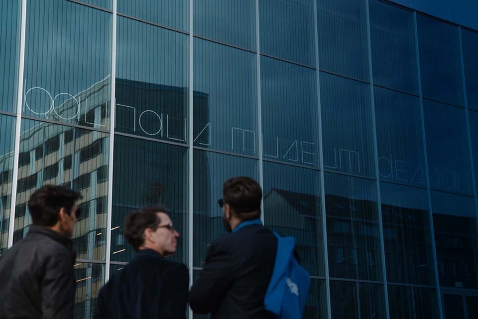 Personas caminando junto a un edificio moderno con fachada de vidrio reflejando el cielo