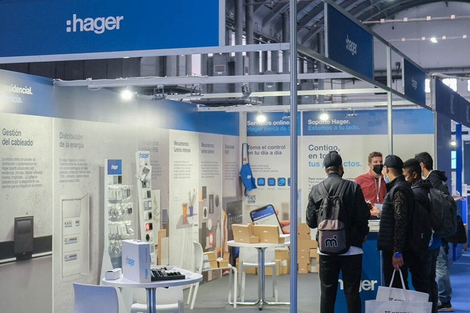 Stand de exposición de la marca Hager mostrando equipos de distribución de energía y interactuando con visitantes en una feria comercial