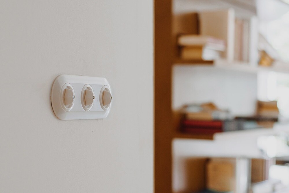 Enchufe triple blanco montado en pared con fondo desenfocado de estantería de libros
