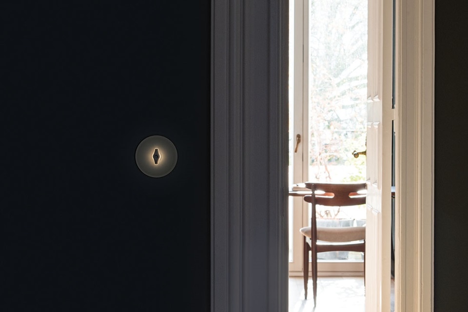 Cerradura iluminada en puerta oscura con vista a una habitación luminosa con sillas